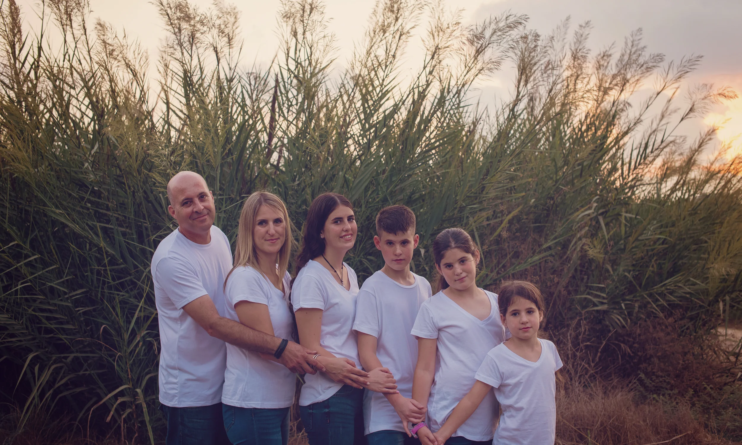 A family standing in tall grass at sunset, on an outdoor shoot near Hadera.