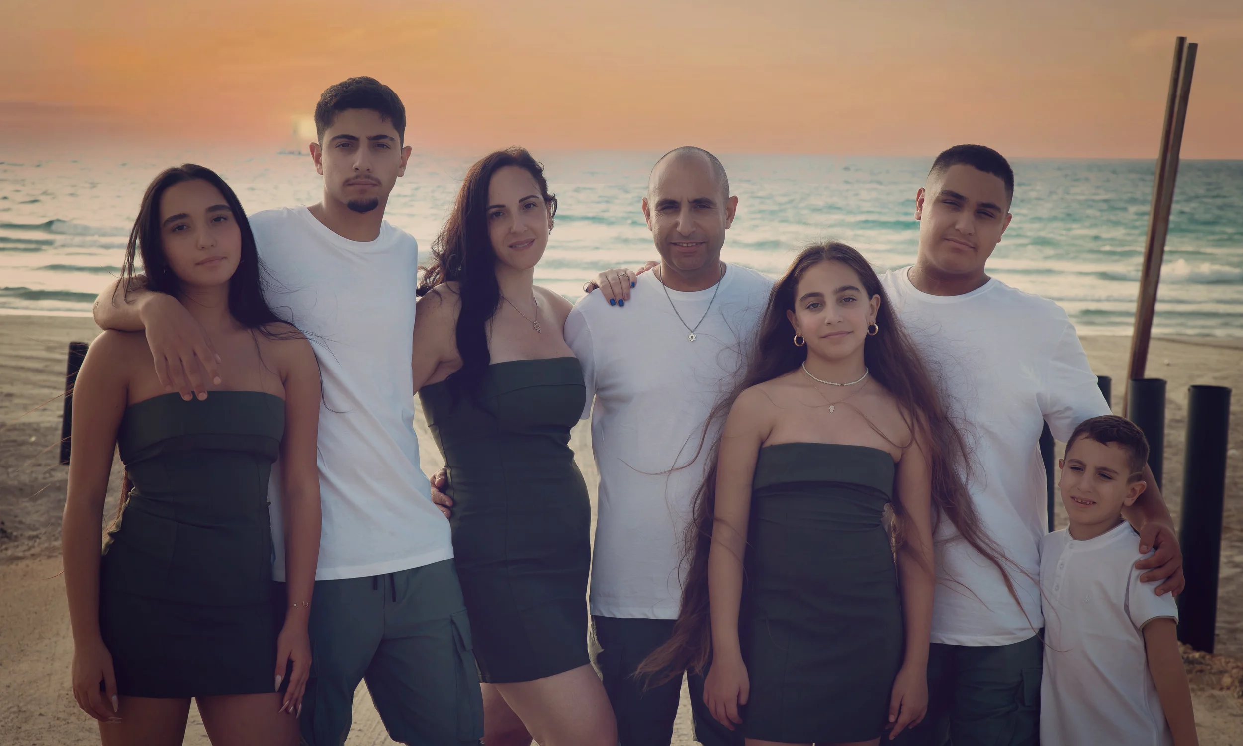 Family standing on a beach at sunset, dressed in white and dark green.